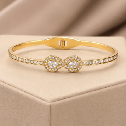 Bracelet jonc doré femme motif infini à deux gouttes en cristal et rangée de pierres claires, sur velours beige