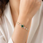 Bracelet doré femme à trèfle vert facetté entouré de strass et pierres claires, porté au poignet
