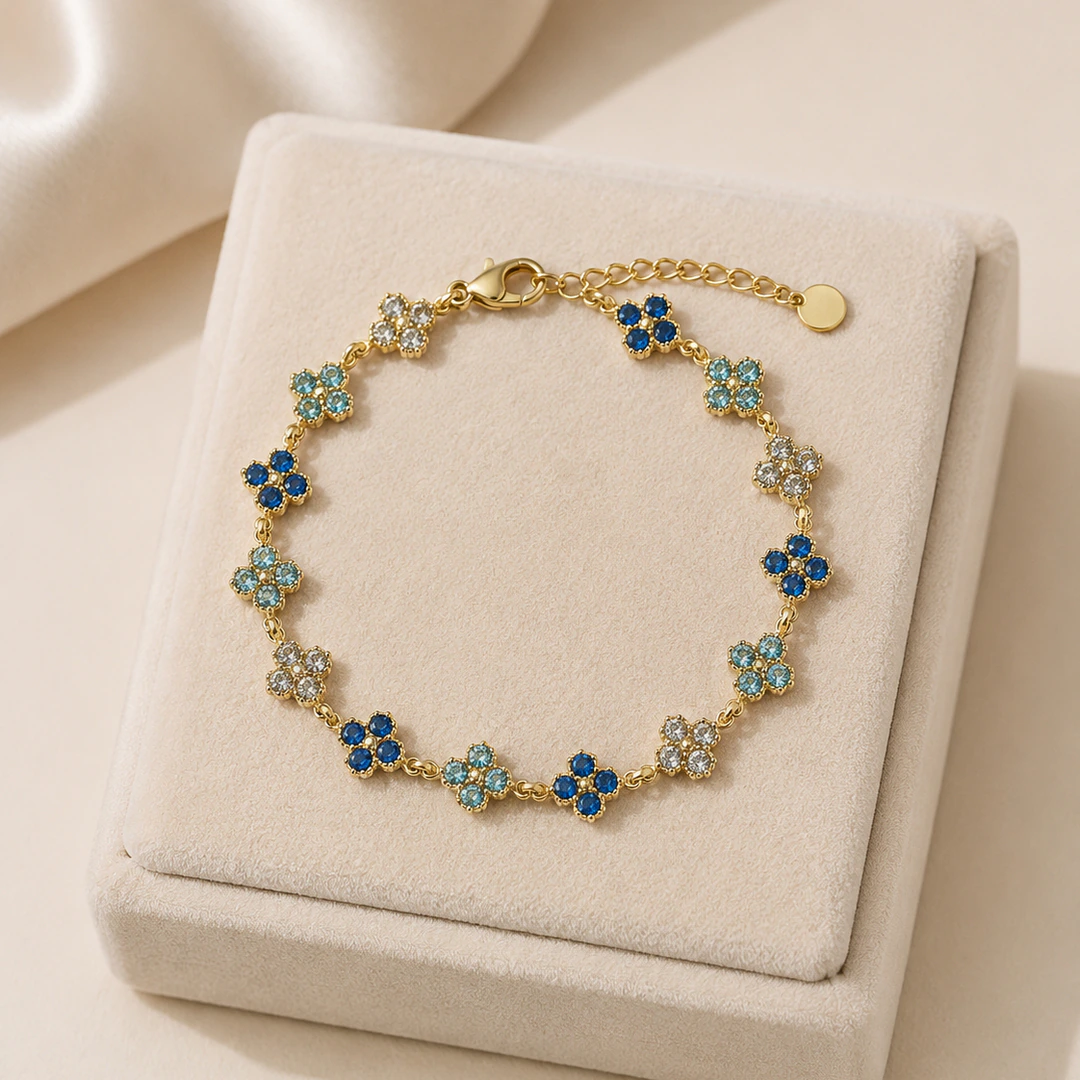 Bracelet doré femme à petits trèfles scintillants en strass bleu nuit, bleu clair et blanc, posé sur un écrin
