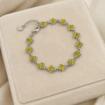 Bracelet argenté femme à trèfles jaunes scintillants en strass posé sur un écrin en velours beige