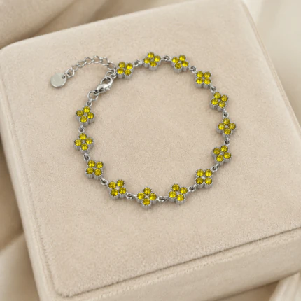 Bracelet argenté femme à trèfles jaunes scintillants en strass posé sur un écrin en velours beige
