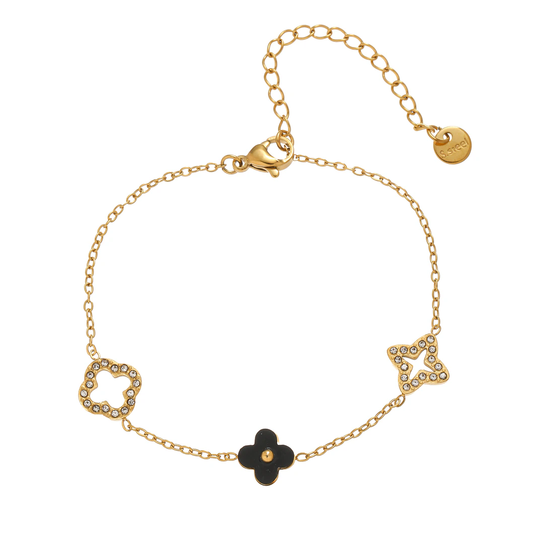 Bracelet doré à trèfle noir central, motifs ajourés sertis de strass et chaînette de rallonge sur fond blanc