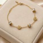Bracelet chaîne fine doré femme à fleurs ajourées et perles serties de strass baguette, sur un écrin