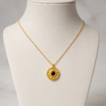 Pendentif médaillon doré gravé à cabochon noir central sur buste de présentation blanc