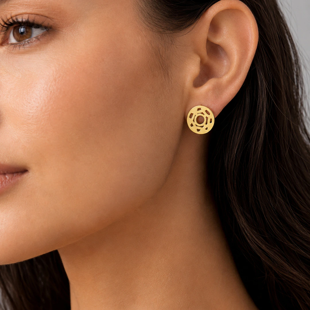 Puce d'oreille ronde dorée ajourée à motif géométrique portée à l'oreille