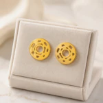 Boucles d'oreilles rondes dorées ajourées à découpes graphiques sur présentoir crème