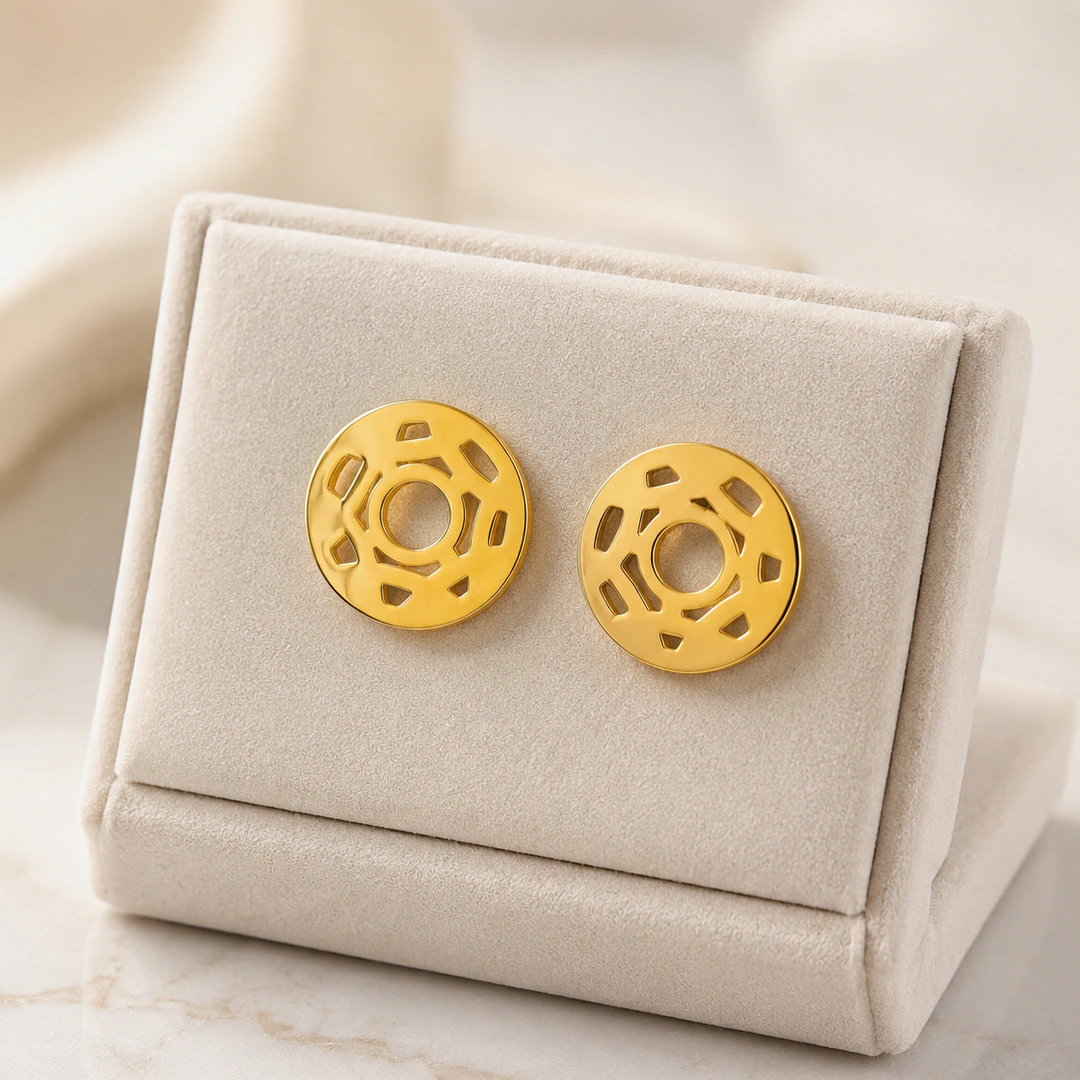 Boucles d'oreilles rondes dorées ajourées à découpes graphiques sur présentoir crème