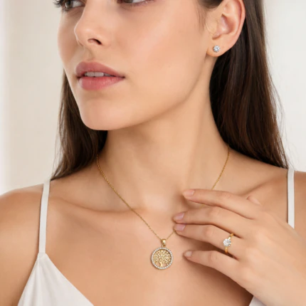 Femme portant un collier arbre de vie doré, une bague solitaire et des puces d'oreilles cristal