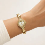 Montre femme dorée à boîtier cœur serti de strass et bracelet maillons cœur portée au poignet