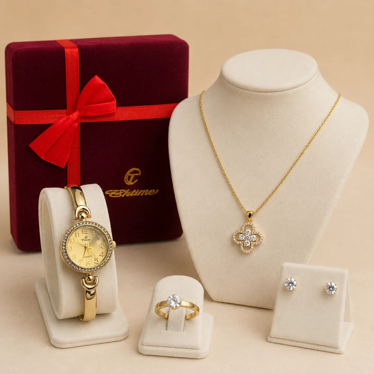 Coffret bijoux femme avec montre dorée, collier pendentif trèfle, bague et puces d'oreilles devant un écrin rouge