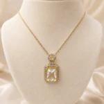 Collier pendentif doré à pierre rectangulaire bordée de strass sur buste de présentation crème