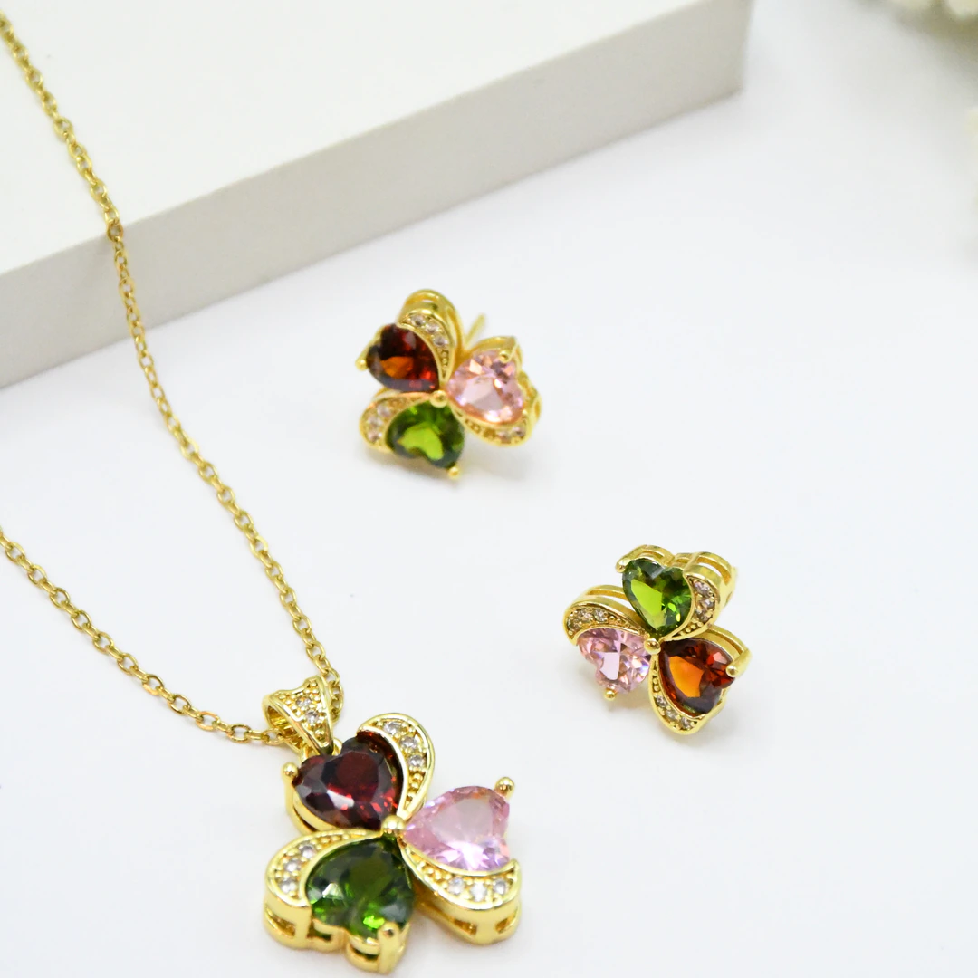 Collier trèfle multicolore doré et puces d'oreilles posés à plat devant un bloc blanc