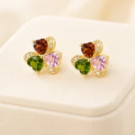 Puces d'oreilles trèfle dorées à cœurs rouge, vert et rose ornées de strass, sur support crème