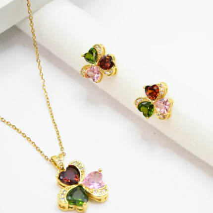 Collier pendentif trèfle multicolore doré et puces d'oreilles assorties posés sur fond blanc