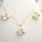 Collier et puces d'oreilles carrés ajourés dorés à cristaux baguette sur présentoir blanc
