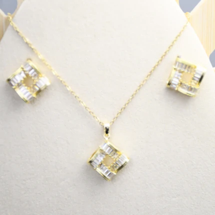 Collier et puces d'oreilles carrés ajourés dorés à cristaux baguette sur présentoir blanc