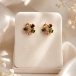 Puces d'oreilles fleur dorées à pétales facettés multicolores sur présentoir crème