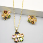 Puces d'oreilles et collier pendentif fleur doré à pétales facettés rose, vert et violet posés à plat