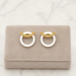 Boucles d'oreilles anneau blanc surmonté d'une barre dorée brillante sur présentoir taupe