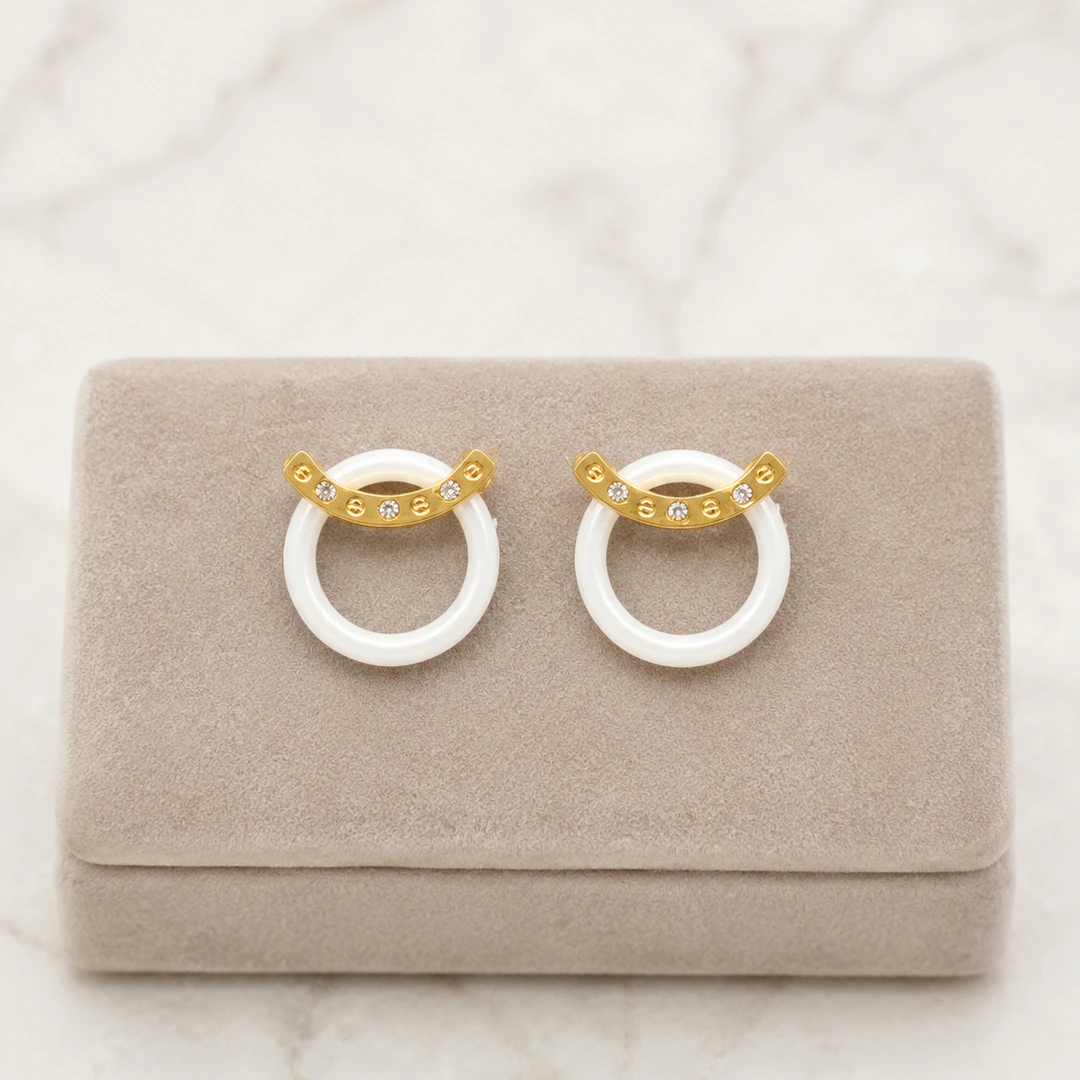 Boucles d'oreilles anneau blanc surmonté d'une barre dorée brillante sur présentoir taupe