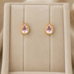Puces d'oreilles dorées à pierre rose en forme de goutte dans un écrin en velours beige