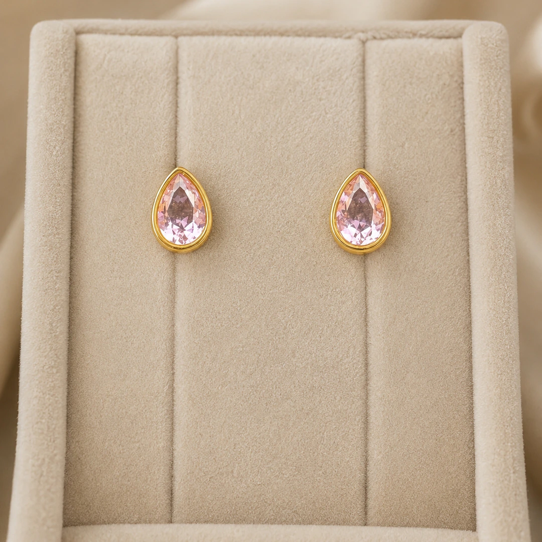Puces d'oreilles dorées à pierre rose en forme de goutte dans un écrin en velours beige