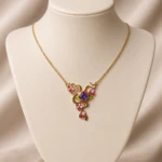 Collier doré à arabesques, fleurs roses et rouges, feuilles vertes et pierre violette en trèfle sur buste