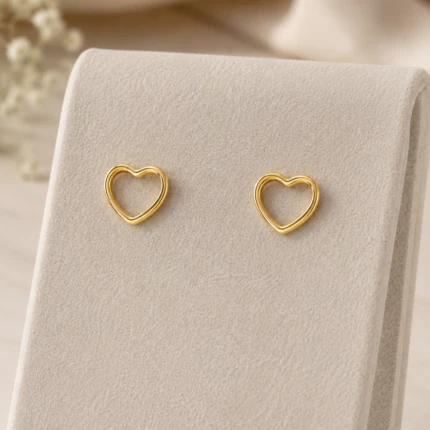 Puces d'oreilles cœur ajouré dorées présentées sur un support en velours beige