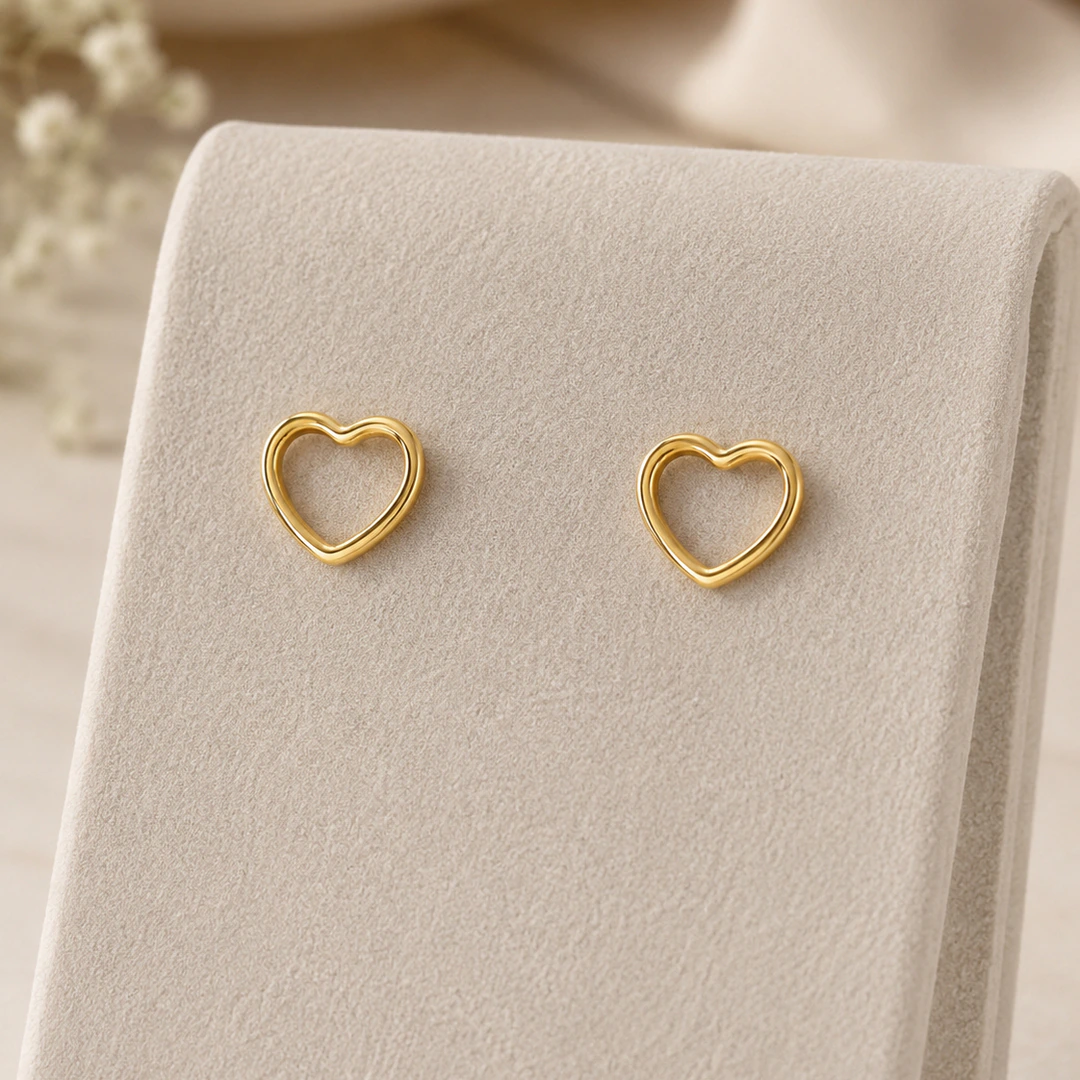 Puces d'oreilles cœur ajouré dorées présentées sur un support en velours beige