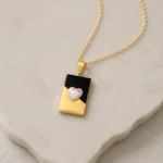 Pendentif rectangulaire doré et noir orné d'un cœur rose nacré posé sur une pierre claire