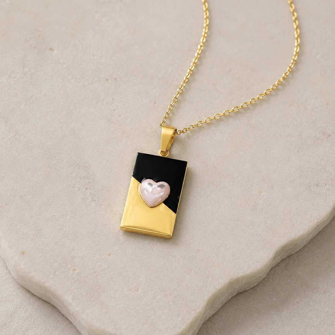 Pendentif rectangulaire doré et noir orné d'un cœur rose nacré posé sur une pierre claire