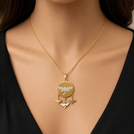 Collier médaillon rond doré orné d'une libellule en strass et de petits papillons, porté au cou
