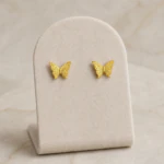 Puces d'oreilles papillon dorées aux ailes ciselées sur présentoir en velours
