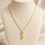 Collier chaîne dorée à pendentif infini vertical pavé de strass sur buste beige