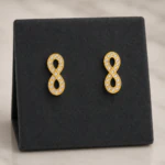 Puces d'oreilles infini dorées serties de strass sur présentoir en velours noir