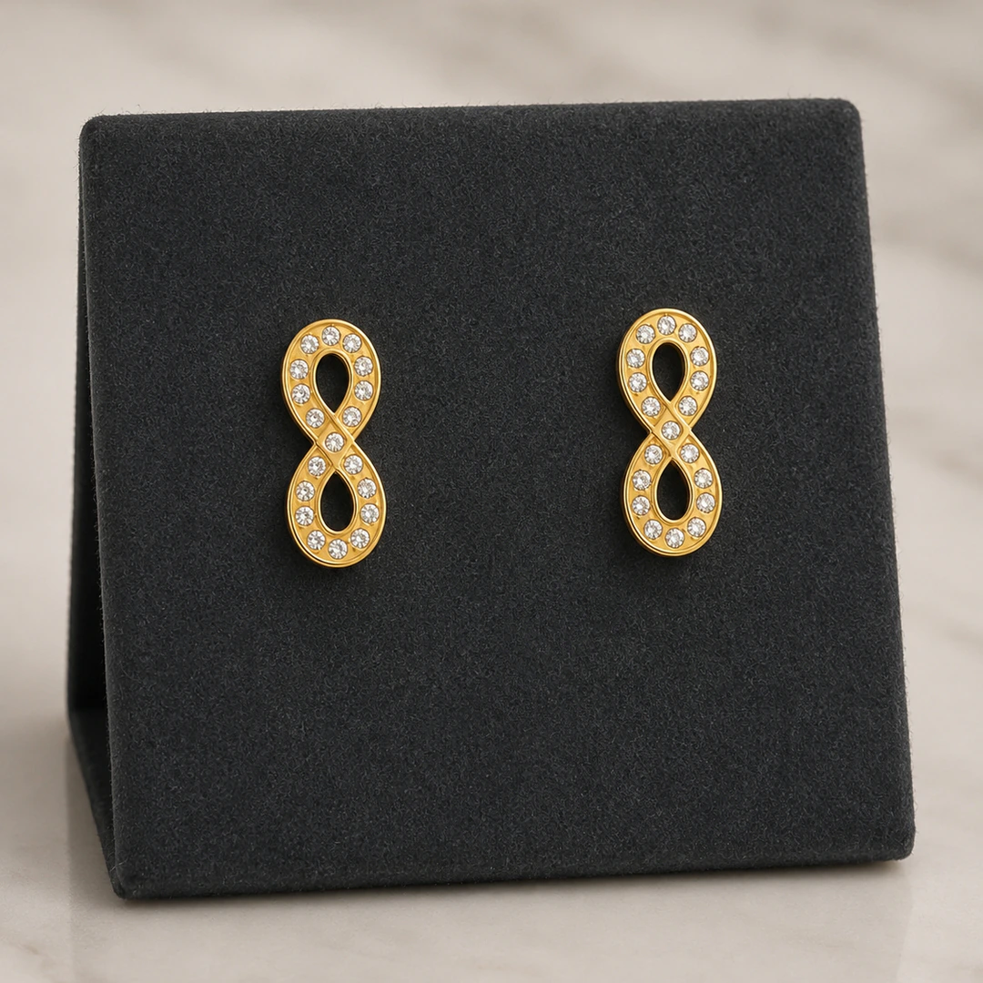 Puces d'oreilles infini dorées serties de strass sur présentoir en velours noir
