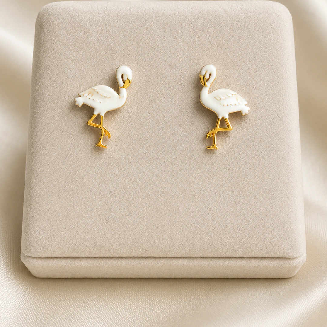 Boucles d'oreilles flamant blanc aux pattes dorées posées sur un présentoir en velours