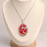 Pendentif ovale argenté pavé de strass rouges à reflets irisés sur buste de présentation