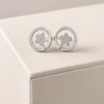 Puces d'oreilles rondes argentées à motif fleur sur tige dans un anneau, posées sur support beige