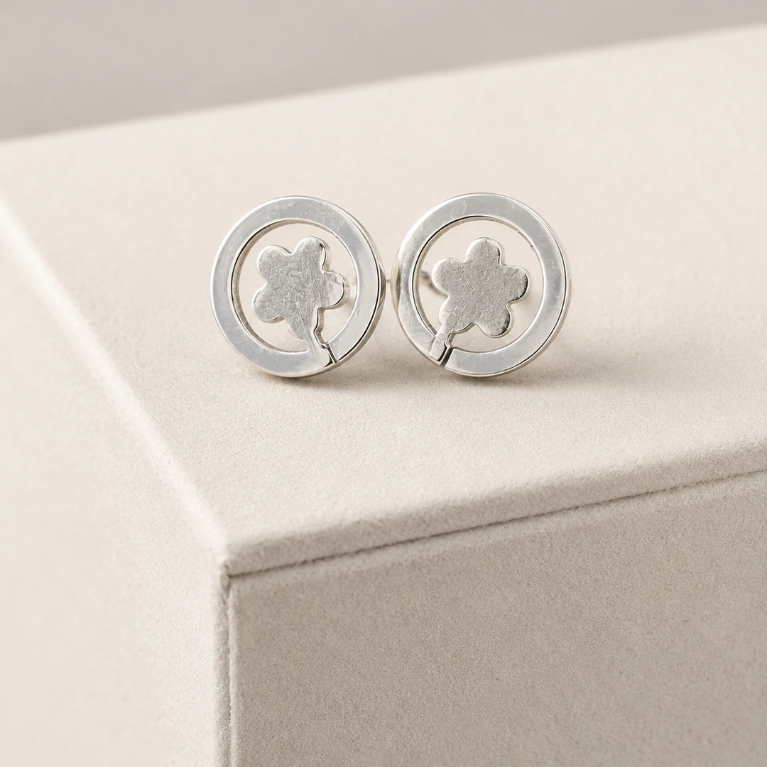 Puces d'oreilles rondes argentées à motif fleur sur tige dans un anneau, posées sur support beige