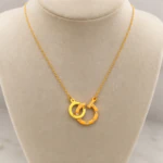Collier chaîne dorée à pendentif anneaux entrelacés ponctués de strass sur buste beige
