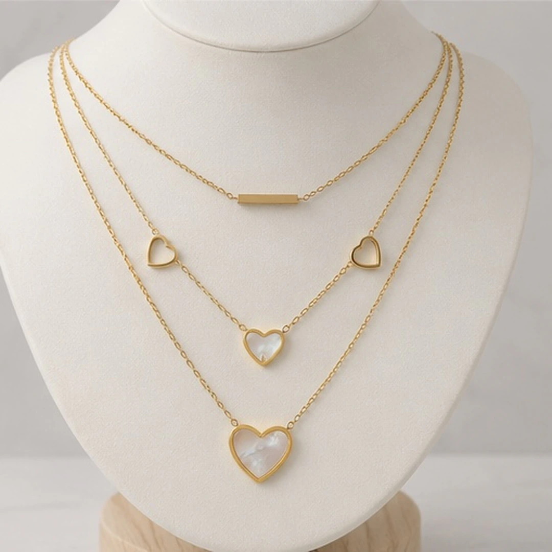 Collier trois rangs doré à barre, cœurs ajourés et cœurs effet nacré sur buste blanc