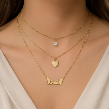 Collier trois rangs doré porté au cou : cristal, pendentif cœur et inscription Smile ailée