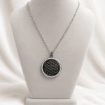 Pendentif rond noir ajouré cerclé de strass sur chaîne argentée, présenté sur buste gris