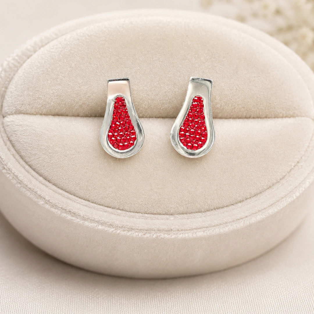 Boucles d'oreilles goutte argentées serties de strass rouges sur coussin en velours crème