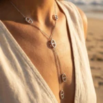 Collier sautoir argenté femme en Y à pendentifs ovales ajourés porté au cou, plage en arrière-plan