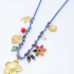 Collier cordon bleu à breloques fleurs dorées, trèfle, oiseau, perle blanche et pierres colorées sur fond blanc