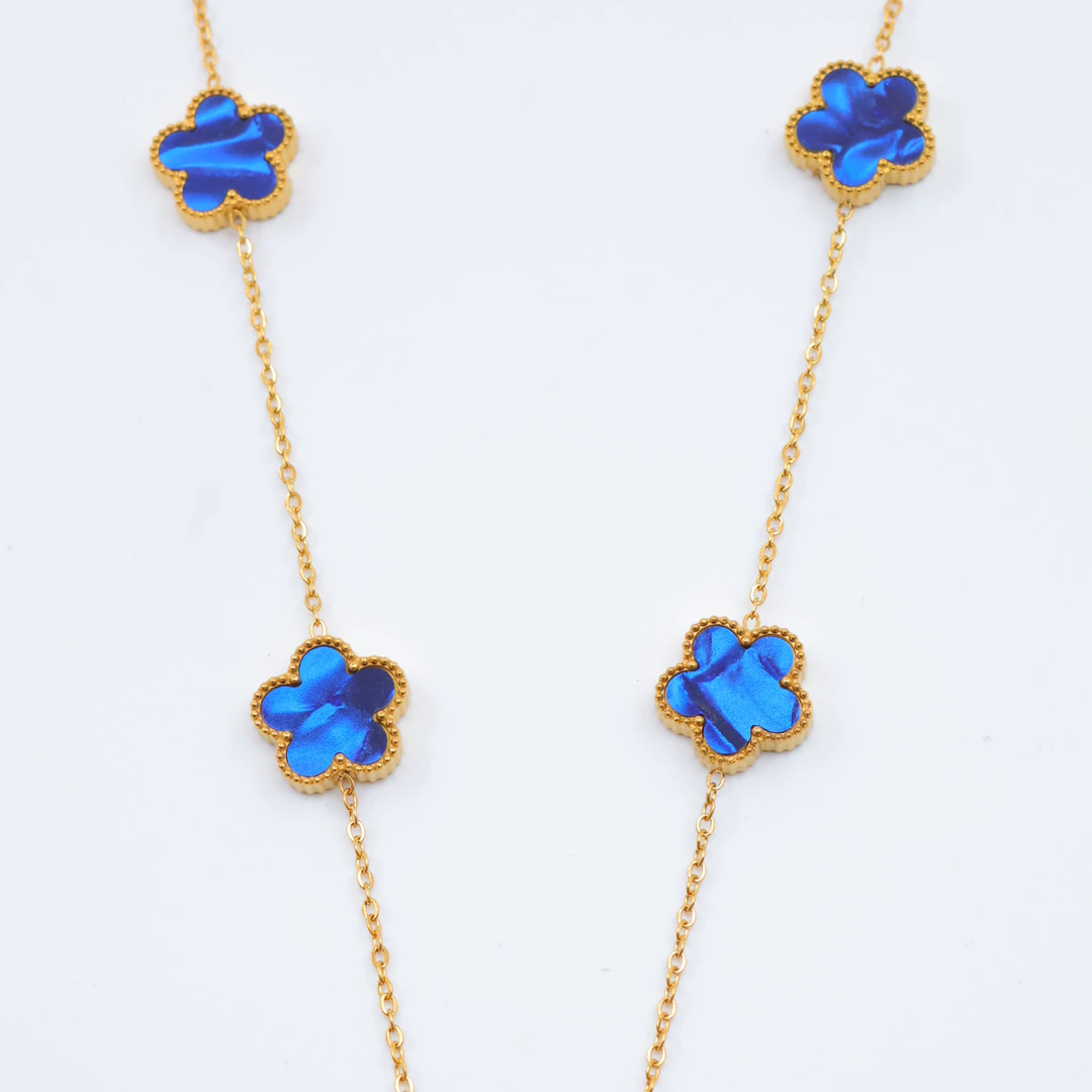 Gros plan sur les trèfles bleu irisé au contour doré perlé et la chaîne fine du collier