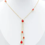 Collier chaîne fine dorée à pierres rouges en forme de goutte et double chute centrale sur buste blanc