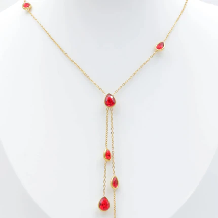 Collier chaîne fine dorée à pierres rouges en forme de goutte et double chute centrale sur buste blanc